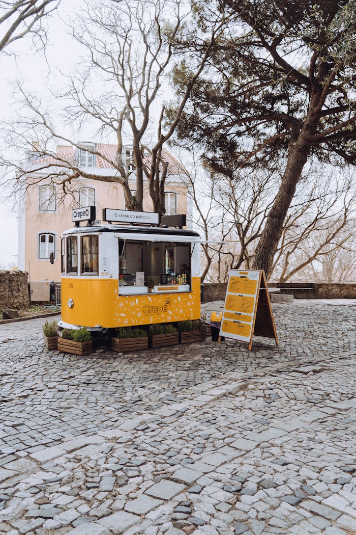 A cozy yellow food stall selling crepes on a serene cobblestone street surrounded by trees.