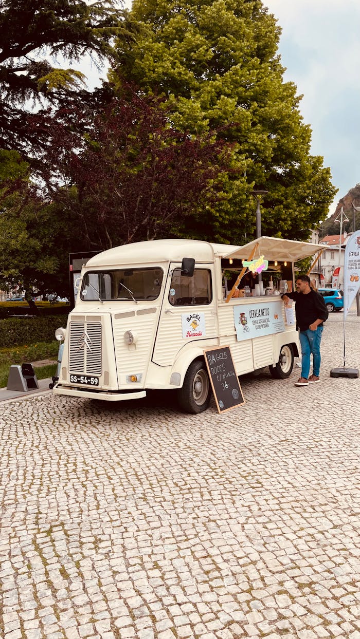 A vintage food truck serves customers on a cobblestone street in a vibrant city setting.